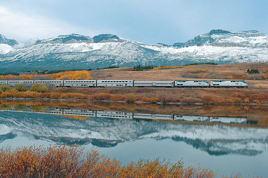 Amtrak train beside water and mountain scenery